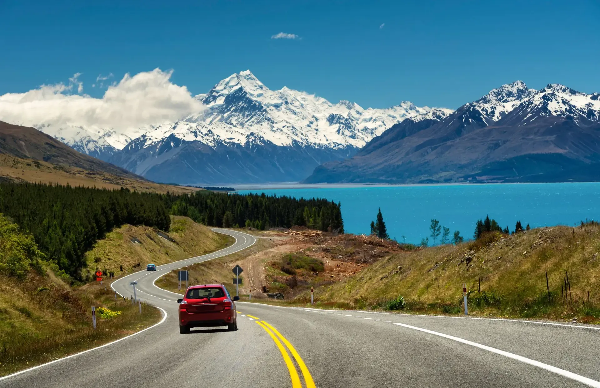 An empty road below Aoraki with one car on it